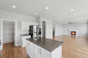 Kitchen with dark stone countertops, a lit fireplace, white cabinetry, stainless steel refrigerator with ice dispenser, and light wood finished floors