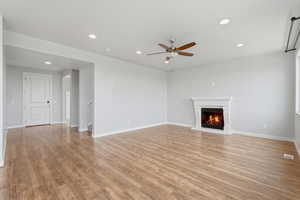 Unfurnished living room with recessed lighting, a warm lit fireplace, light wood-style floors, and ceiling fan