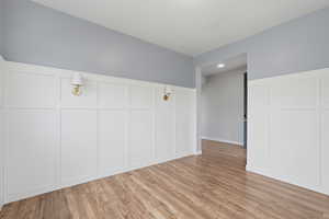 Unfurnished bedroom featuring a decorative wall, a wainscoted wall, and light wood-type flooring