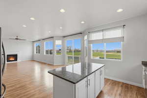 Kitchen featuring a glass covered fireplace, dark stone counters, a center island, light wood-style flooring, and white cabinets