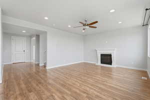 Unfurnished living room featuring recessed lighting, light wood finished floors, a ceiling fan, and a glass covered fireplace