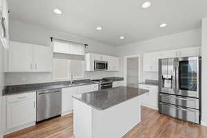 Kitchen with stainless steel appliances, white cabinets, dark stone countertops, light wood-style flooring, and recessed lighting