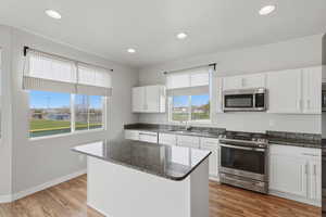 Kitchen with stainless steel appliances, dark stone counters, light wood finished floors, white cabinetry, and recessed lighting