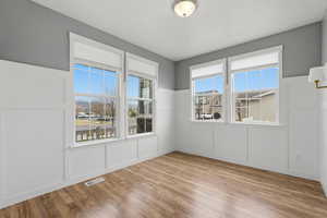 Unfurnished room featuring a decorative wall, wainscoting, light wood-style floors, and plenty of natural light