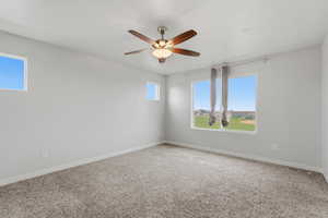 Carpeted spare room featuring healthy amount of natural light and a ceiling fan
