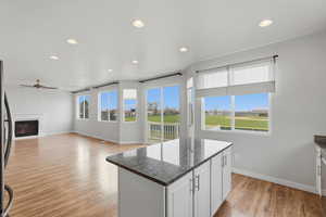 Kitchen with dark stone counters, a kitchen island, white cabinets, light wood-style flooring, and a glass covered fireplace