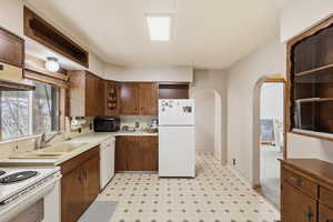 Kitchen featuring light flooring, white appliances, arched walkways, open shelves, and light countertops