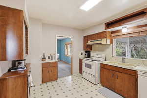 Kitchen with light floors, white appliances, wood finish cabinetry, and healthy amount of natural light
