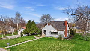 Bungalow-style house featuring a front lawn, a chimney, roof with shingles, and an outbuilding