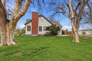 View of side of home featuring a lawn, a chimney, and roof with shingles