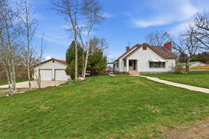 View of home's exterior featuring a lawn, a chimney, an outbuilding, and concrete driveway