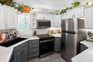 Kitchen with stainless steel appliances, light countertops, open shelves, and gray cabinetry