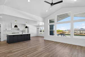 Two tone kitchen with suspended lighting, ceiling fan, open floor plan, a center island with sink, and dark wood-style flooring