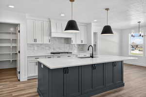 Two tone kitchen featuring light stone countertops, light wood-type flooring, tasteful backsplash, two tone color scheme, and a center island with sink