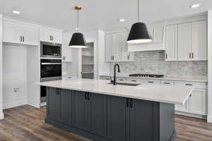 Kitchen with two tone cabinetry, light stone counters, a kitchen island with sink, stainless steel appliances, and dark wood-type flooring