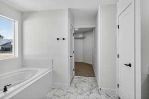 Bathroom featuring a bath, light marble finish flooring, and a textured ceiling