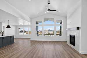 Unfurnished living room featuring a tile fireplace, ceiling fan, dark wood-type flooring, a high textured ceiling, and suspended lighting
