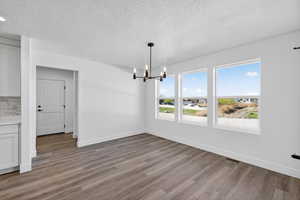 Unfurnished dining area with a chandelier, dark wood finished floors, and a textured ceiling