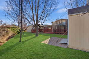 View of grassy yard featuring a wooden deck, a patio, and a shed