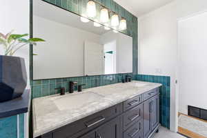 Bathroom featuring double vanity, ornamental molding, and tile walls