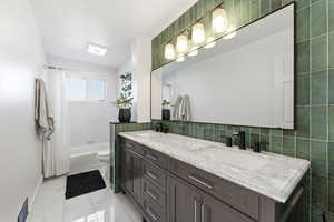 Full bathroom featuring double vanity, shower / bath combo with shower curtain, and light marble finish floors