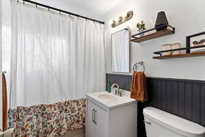 Bathroom with curtained shower, vanity, and a wainscoted wall
