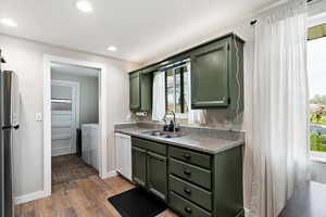 Kitchen featuring green cabinetry, freestanding refrigerator, dark wood-style flooring, dishwasher, and washer and dryer