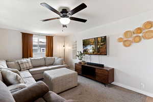 Carpeted living room featuring baseboards and a ceiling fan