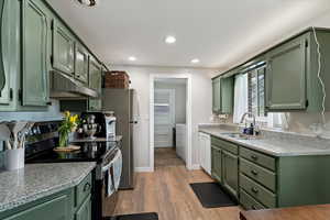 Kitchen with green cabinetry, stainless steel range with electric stovetop, dark wood-style floors, recessed lighting, and light stone countertops
