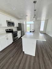 Kitchen with stainless steel appliances, an island with sink, dark wood-style floors, white cabinetry, and pendant lighting