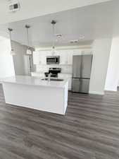 Kitchen featuring stainless steel appliances, white cabinets, decorative light fixtures, a kitchen island with sink, and a textured ceiling