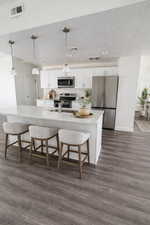 Kitchen featuring white cabinetry, stainless steel appliances, a breakfast bar, pendant lighting, and a textured ceiling