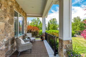 Covered porch with natural stone facade, composite decking, white architectural columns, black iron railing, and a beadboard ceiling