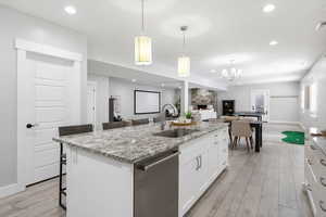 Full kitchen featuring light stone counters, a kitchen breakfast bar, dishwasher, white cabinets, and an island with sink