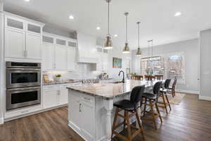 Kitchen featuring stainless steel double oven, a spacious island, light stone counters, a breakfast bar area, and dark wood-style flooring