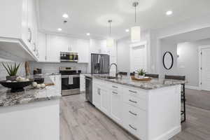 Full kitchen with light stone counters, white cabinetry, a kitchen bar, stainless steel appliances, and light wood finished floors