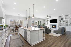 Kitchen featuring white cabinetry, a glass covered fireplace, light stone counters, a breakfast bar area, and dark wood finished floors