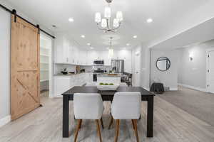 Dining space with a barn door leading into a large pantry, light wood-style flooring, and a chandelier