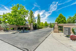 Brick entrance walls with wrought iron gates, mature landscaping, and an asphalt road