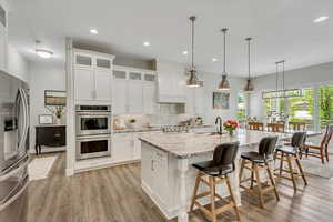 Kitchen featuring glass fronted cabinets, light stone countertops, stainless steel appliances, a kitchen breakfast bar, and white cabinetry