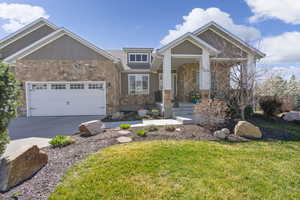 Craftsman-style home with stone siding, concrete driveway, a garage, and a front lawn