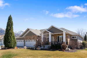 Craftsman-style home featuring stone siding, a front yard, a porch, and an attached garage