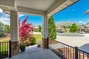 Covered porch featuring stone-clad pillars, a concrete surface, and black metal railings