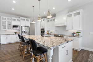 Kitchen featuring glass fronted cabinets, a kitchen breakfast bar, light stone countertops, and dark wood-style flooring