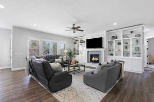 Living room with ceiling fan, dark wood-type flooring, a fireplace, and recessed lighting