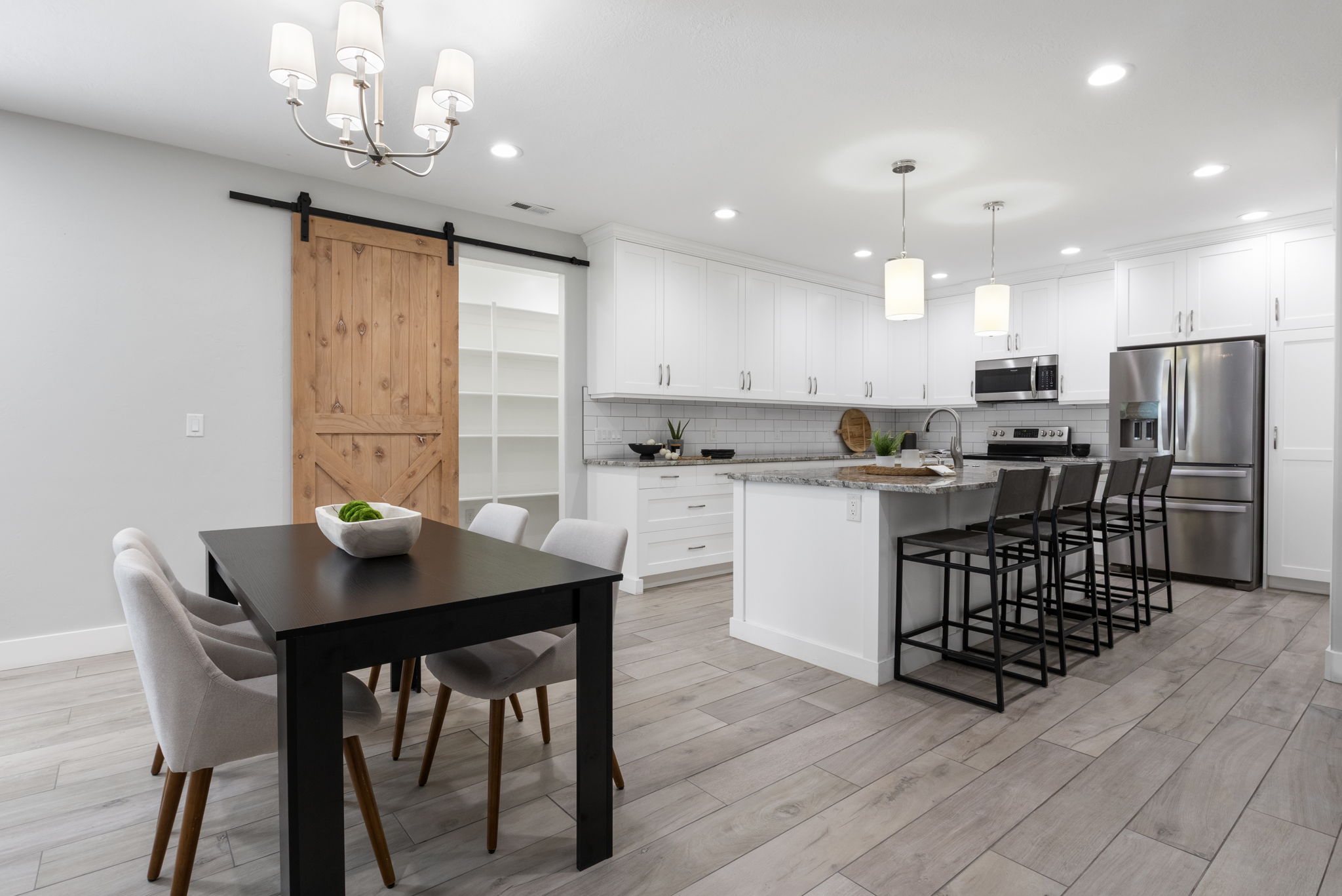 Kitchen featuring a pantry, stainless steel appliances, light stone counters, a kitchen breakfast bar, and white cabinetry