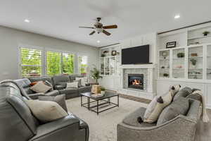 Living area featuring ceiling fan, wood finished floors, built in shelves, a glass covered fireplace, and recessed lighting