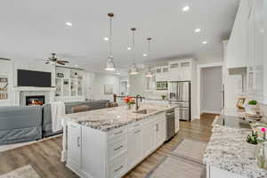 Kitchen featuring open floor plan, white cabinetry, light stone counters, and stainless steel appliances