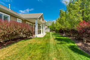 Spacious side yard featuring a manicured lawn, established shrubbery, and mature trees