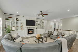 Living area featuring light wood-type flooring, a fireplace, ceiling fan, built in shelves, and recessed lighting
